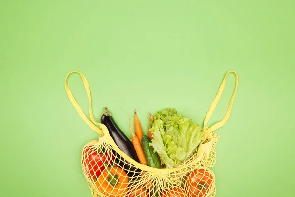 Top view of yellow string bag with organic vegetables on light green surface with copy space — Stock Photo