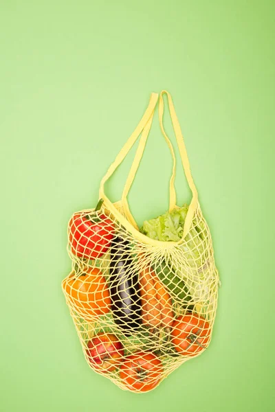 Vue du dessus du sac à ficelle jaune avec des légumes biologiques mûrs sur une surface vert clair avec espace de copie — Photo de stock