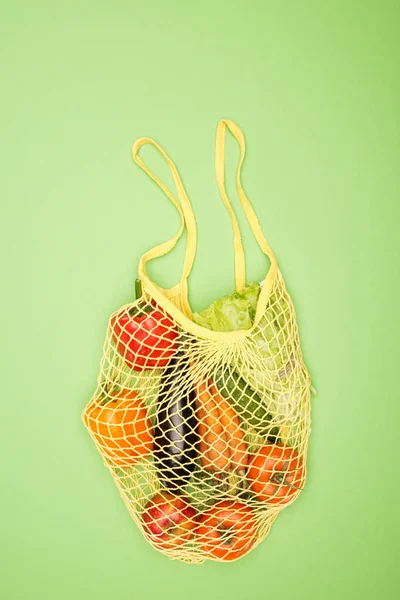 Top view of yellow string bag with ripe organic vegetables on light green surface — Stock Photo