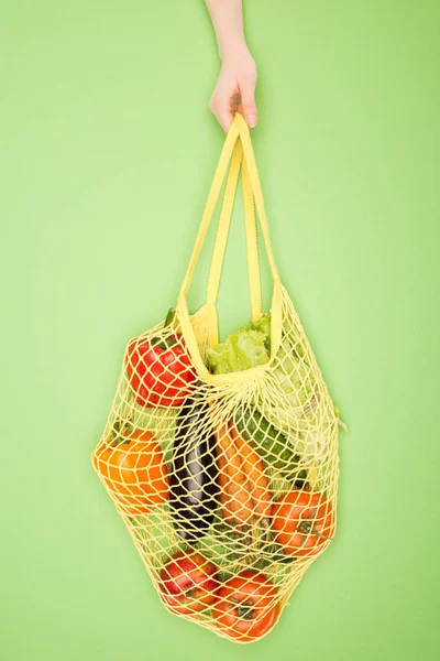 Partial view of woman holding string bag with vegetables on light green — Stock Photo