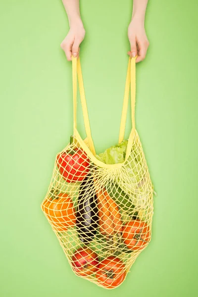 Cropped view of woman holding string bag with vegetables on light green — Stock Photo