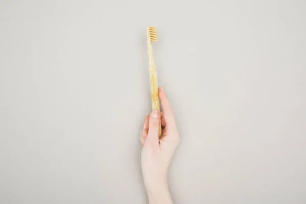 Partial view of woman holding bamboo toothbrush on grey background — Stock Photo