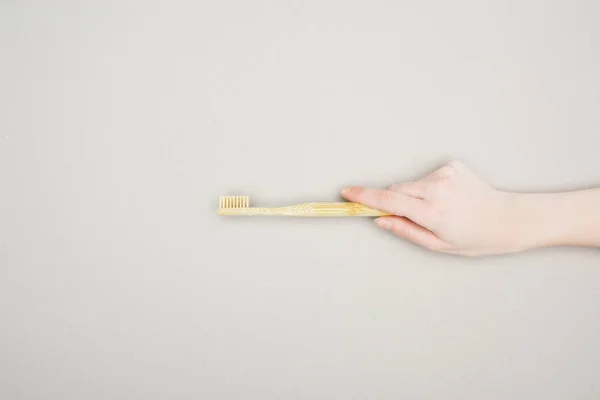 Vista recortada de la mujer sosteniendo el cepillo de dientes de bambú sobre fondo gris - foto de stock