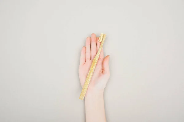 Обрізаний вид жінки, що тримає бамбукову зубну щітку в долоні на сірому фоні — стокове фото