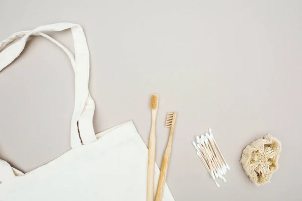 Wooden toothbrushes, organic loofah, cotton swabs and white cotton bag on grey background — Stock Photo