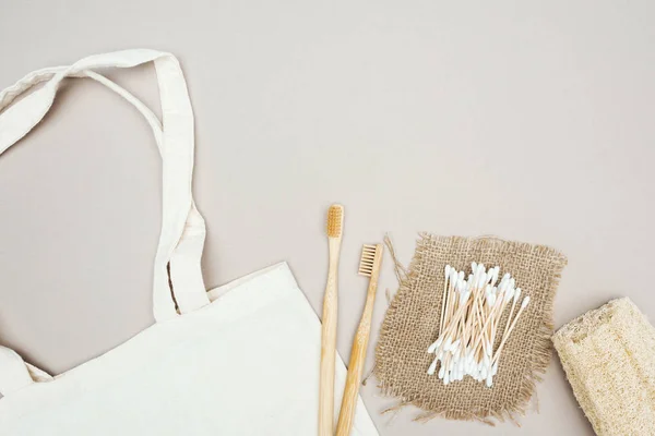 Brosses à dents en bois, loofah bio, coton-tige, sac à dos et sac en coton blanc sur fond gris — Photo de stock