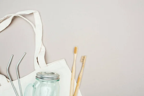 Bamboo toothbrushes, reusable stainless steel straws and glass jar on white cotton bag — Stock Photo