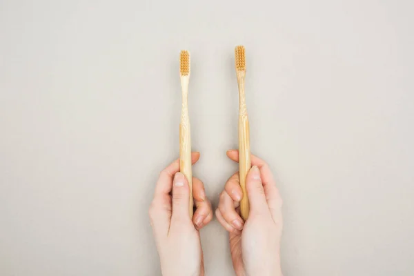 Vista recortada de la mujer sosteniendo cepillos de dientes de bambú en las manos sobre fondo gris - foto de stock