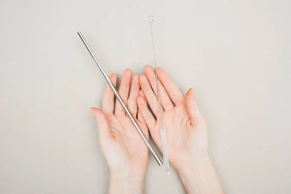 Teilansicht einer Frau mit Putzbürste und Edelstahlstroh in der Hand auf grau — Stockfoto