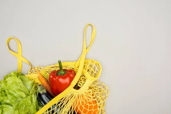 Yellow string bag with fresh ripe vegetables on grey background — Stock Photo