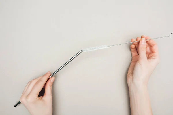 Partial view of woman holding cleaning brush and stainless steel straw on grey — Stock Photo