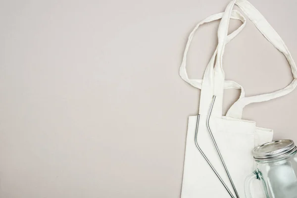 Vista superior do saco de algodão branco, frasco de vidro e palhas de aço inoxidável reutilizáveis no fundo cinza — Stock Photo
