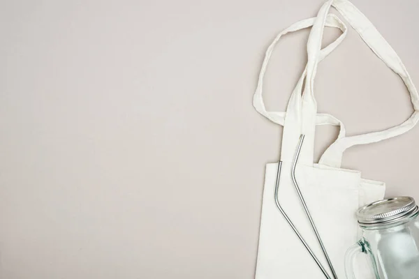 Top view of white cotton bag, glass jar and reusable stainless steel straws on grey background — Stock Photo