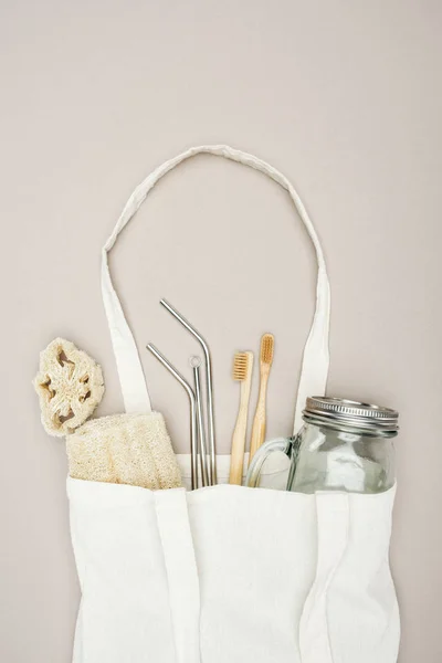 Bamboo toothbrushes, organic loofah, jar and stainless steel straws in white cotton bag on grey background — Stock Photo