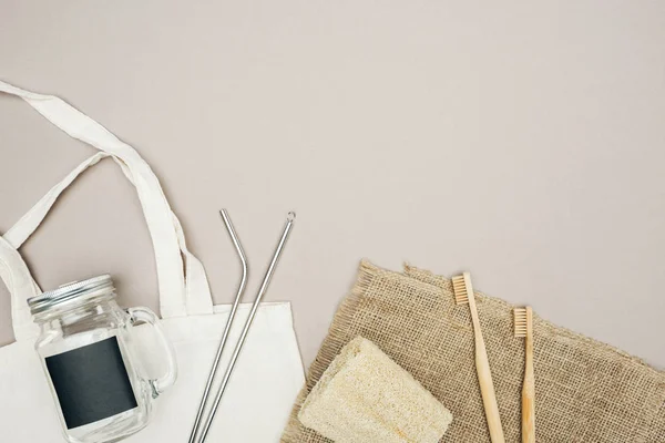 Bamboo toothbrushes, organic loofah, brown sackcloth, cotton bag with jar and stainless steel straws on grey background — Stock Photo