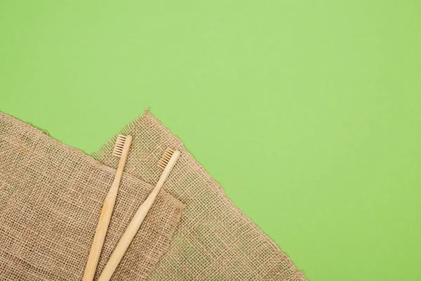 Escovas de dentes de bambu e pano de saco marrom no fundo verde claro — Fotografia de Stock