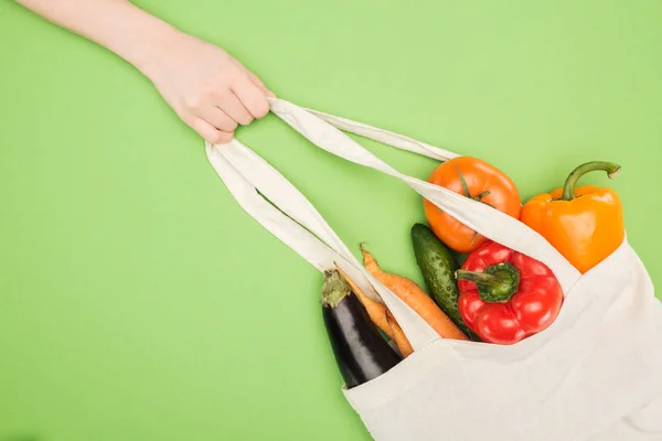 Vista parcial de la mujer sosteniendo la manija de la bolsa de algodón llena de verduras maduras - foto de stock