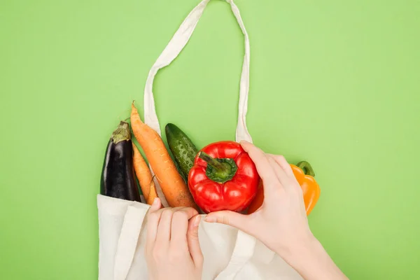 Vista parcial de la mujer poniendo colorido pimiento en bolsa de algodón con verduras sobre fondo verde claro - foto de stock