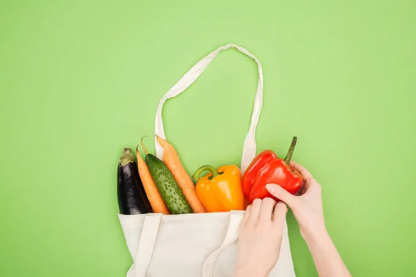 Vista recortada de la mujer poniendo verduras de colores en bolsa de algodón sobre fondo verde claro - foto de stock