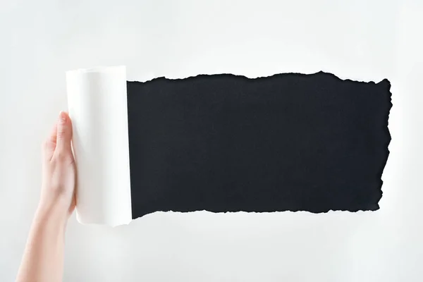 Cropped view of woman holding textured white paper with rolled edge on black background — Stock Photo