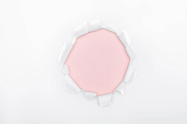 Ragged hole in textured white paper on pink background — Stock Photo