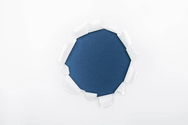 Ragged hole in textured white paper on dark blue background — Stock Photo