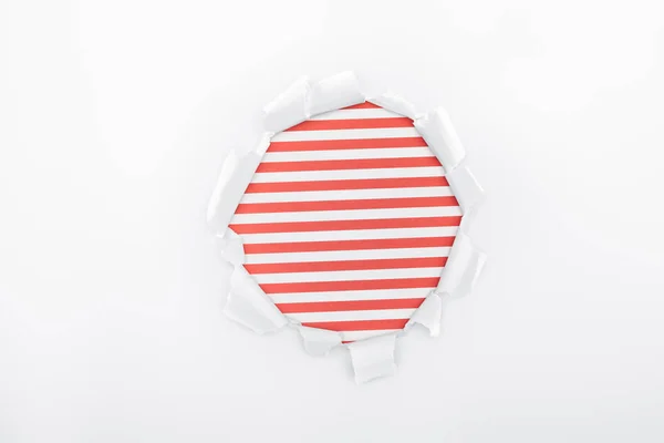 Ragged hole in textured white paper on red striped background — Stock Photo