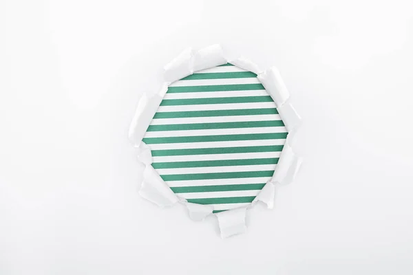 Agujero irregular en papel blanco texturizado sobre fondo rayado verde - foto de stock