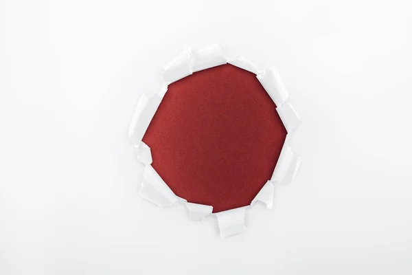 Ragged hole in textured white paper on burgundy background — Stock Photo