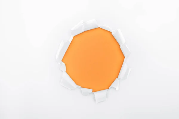 Ripped hole in textured white paper on orange background — Stock Photo