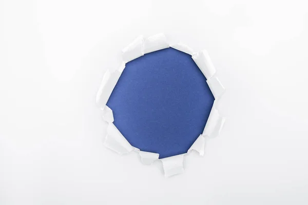 Buco strappato in carta bianca strutturata su sfondo blu — Foto stock