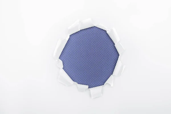 Trou déchiré dans du papier blanc texturé sur fond bleu pointillé — Photo de stock