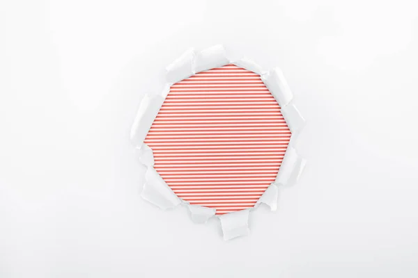 Agujero rasgado en papel blanco texturizado sobre fondo rayado rojo - foto de stock