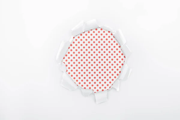 Buco strappato in carta bianca strutturata su sfondo a pois rosso — Foto stock