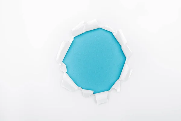 Buraco esfarrapado em papel branco texturizado em fundo azul — Fotografia de Stock