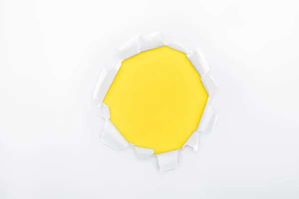 Torn hole in white textured paper on yellow background — Stock Photo