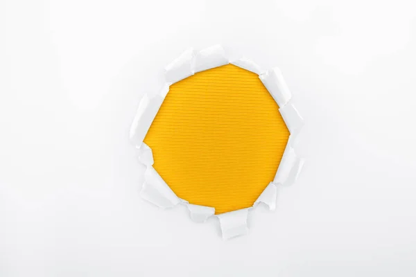 Agujero rasgado en papel texturizado blanco sobre fondo rayado naranja - foto de stock