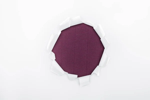 Torn hole in white textured paper on purple background — Stock Photo