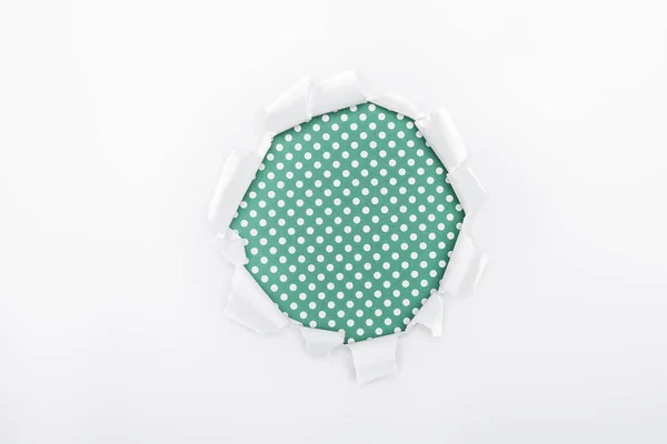 Torn hole in white textured paper on green dotted background — Stock Photo