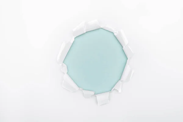 Ripped  hole in white textured paper on light blue dotted background — Stock Photo