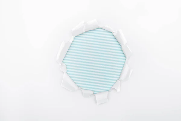 Torn hole in white textured paper on light blue striped background — Stock Photo