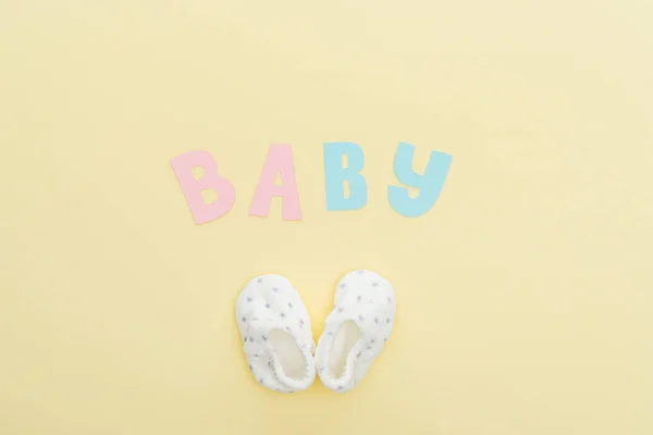 Top view of booties and baby lettering isolated on yellow — Stock Photo