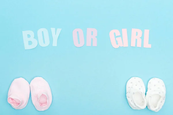 Top view of booties and boy or girl lettering on blue background with copy space — Stock Photo