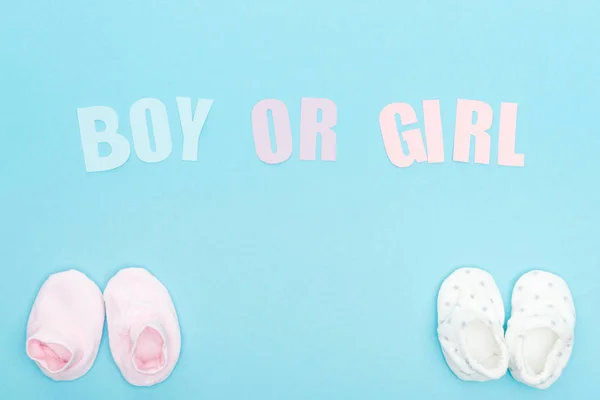 Vista superior de botines y letras de niño o niña sobre fondo azul con espacio para copiar - foto de stock