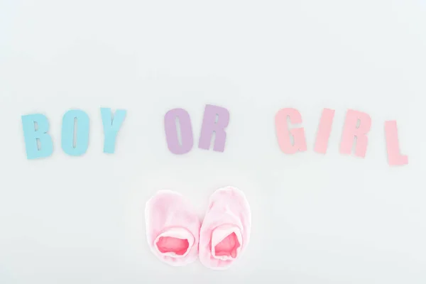 Top view of pink booties and boy or girl lettering isolated on white with copy space — Stock Photo