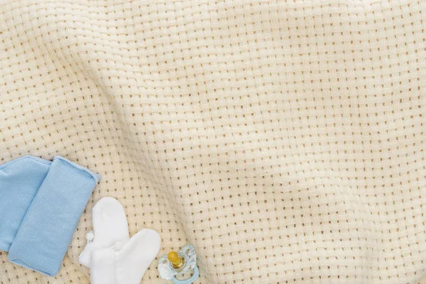 Top view of pacifier, hat, booties on beige blanket with copy space — Stock Photo