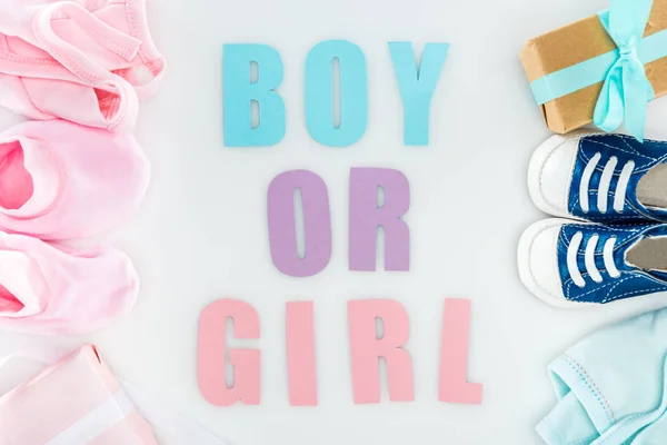 Top view of booties and sneakers, boy or girl lettering, gift boxes and bonnets — Stock Photo