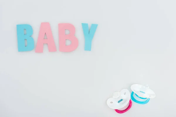 Top view of pacifiers and pink and blue baby lettering isolated on white with copy space — Stock Photo