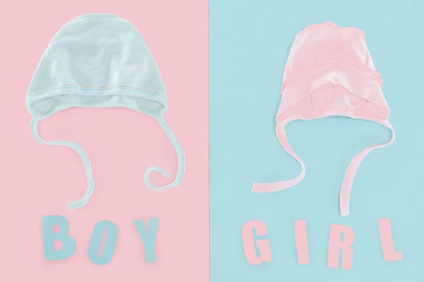 Top view of boy and girl lettering, bonnets on pink and blue background — Stock Photo