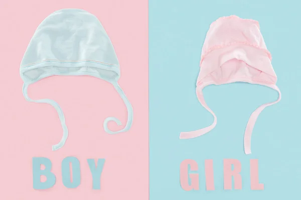 Top view of boy and girl lettering, bonnets on pink and blue background — Stock Photo